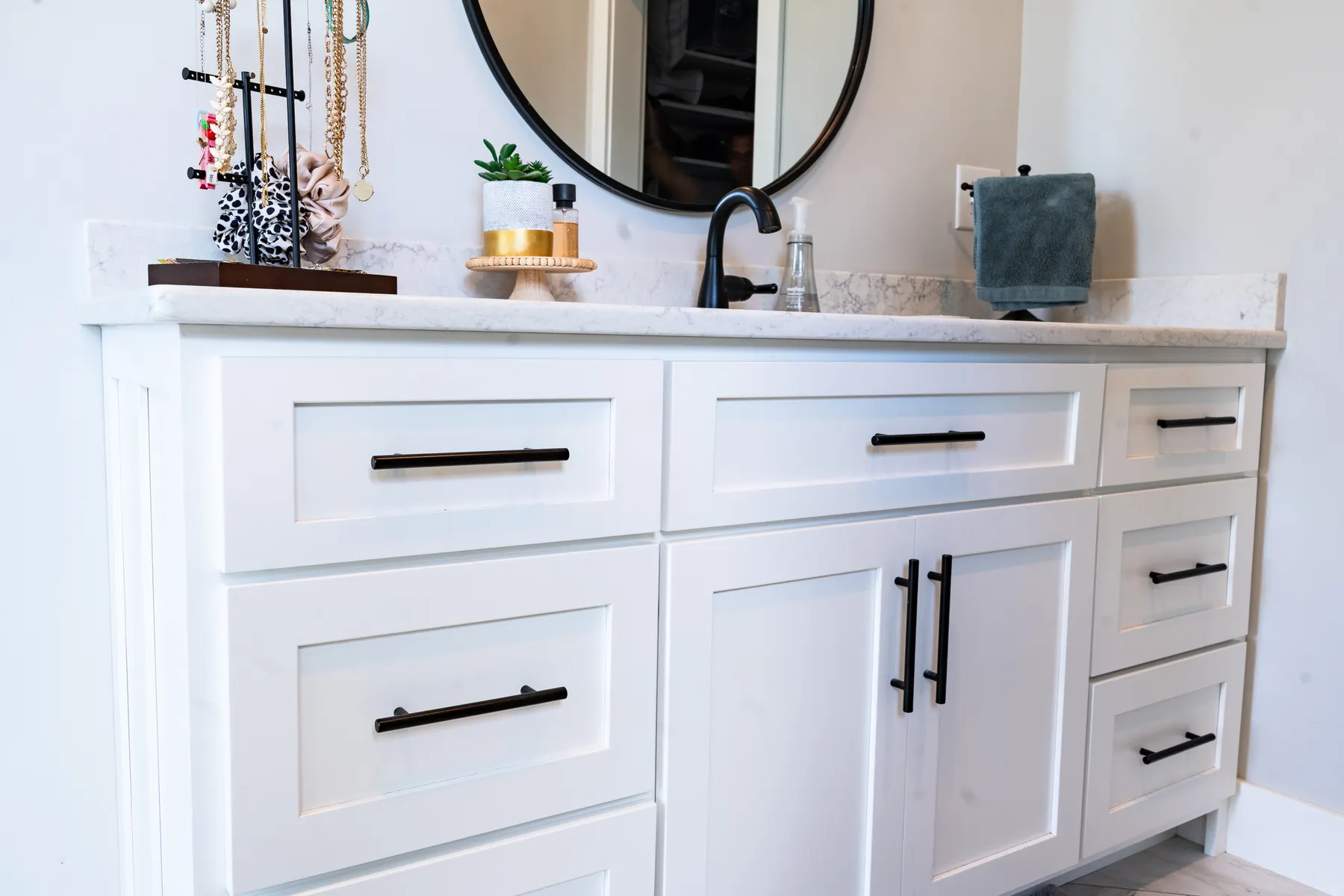 White bathroom vanity with black hardware and a round black-framed mirror