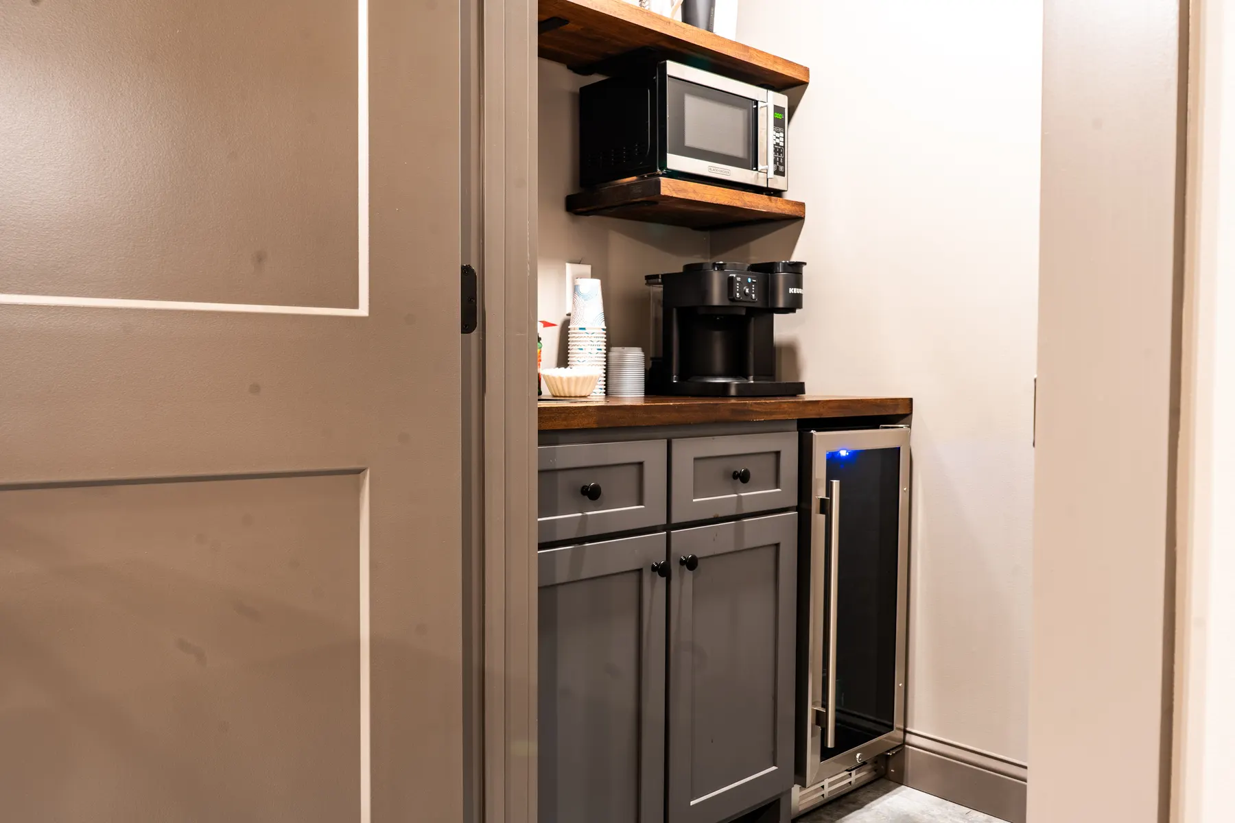 Gray coffee-bar cabinets with wood shelves and a beverage cooler