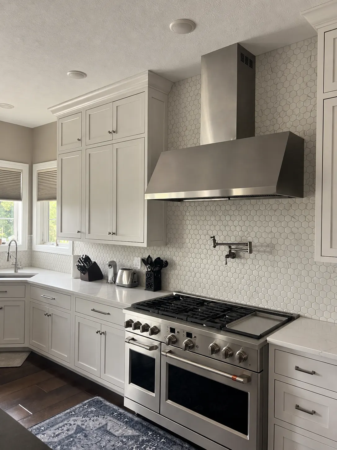White kitchen cabinets around a stainless range and hexagonal tile backsplash