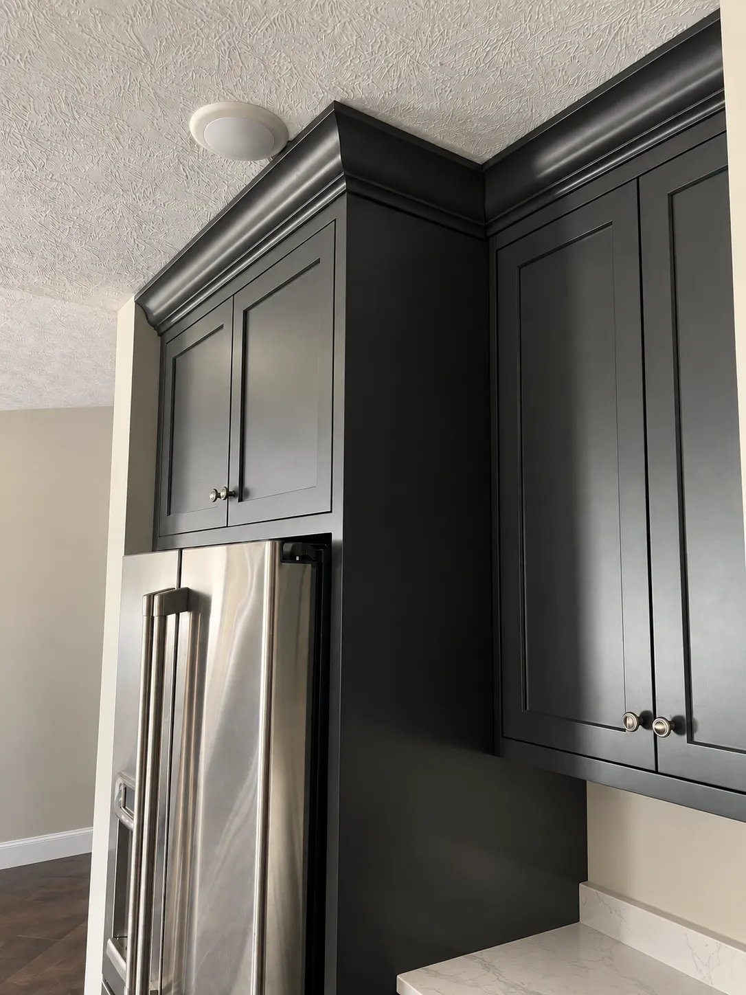 Dark painted cabinets wrapping a stainless refrigerator