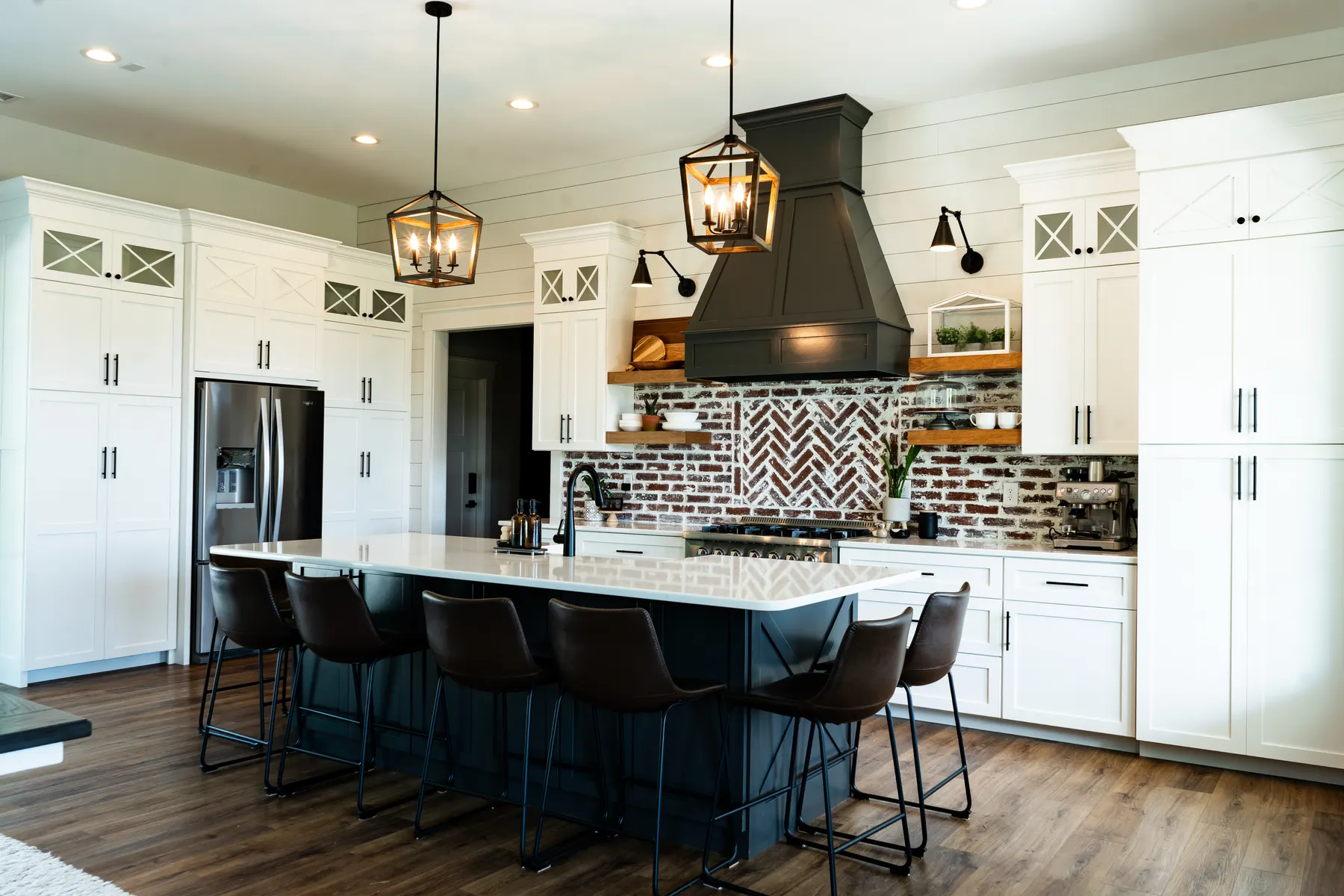 White shaker kitchen with a dark island, brick backsplash, and black range hood
