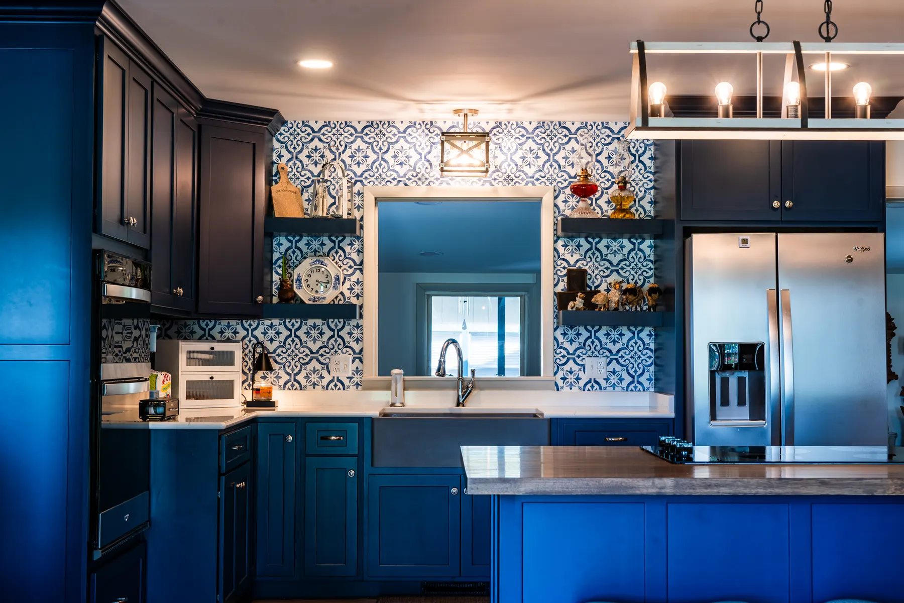 Navy shaker cabinets with a stainless farmhouse sink and blue-and-white tile backsplash